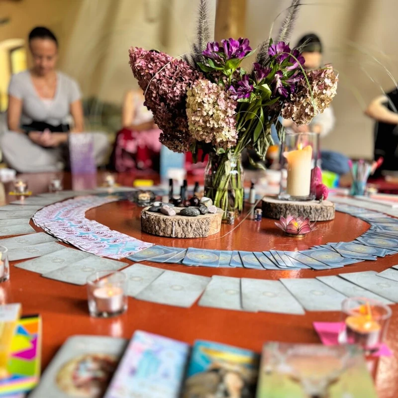 Środek kręgu na rudej podłodze: hortensje, świeca i spirala kart, w tle kobiety w kręgu